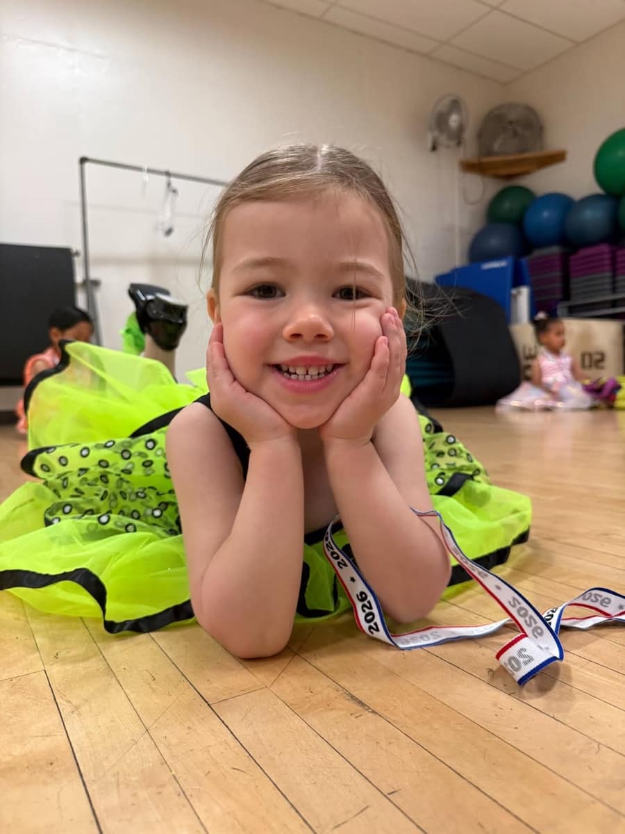 Young dancer in a neon green tutu smiling on the studio floor