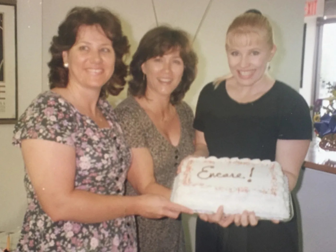 Raynor van der Merwe with two colleagues holding an Encore cake in the studio's founding year