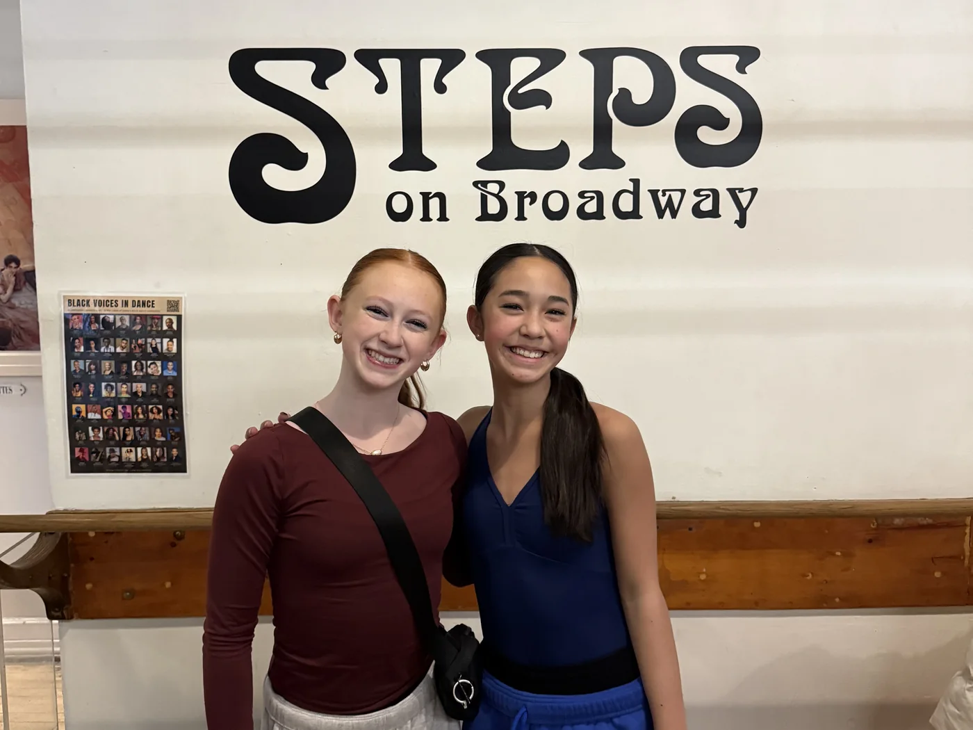 Two Encore dancers together under the Steps on Broadway sign in the New York studio
