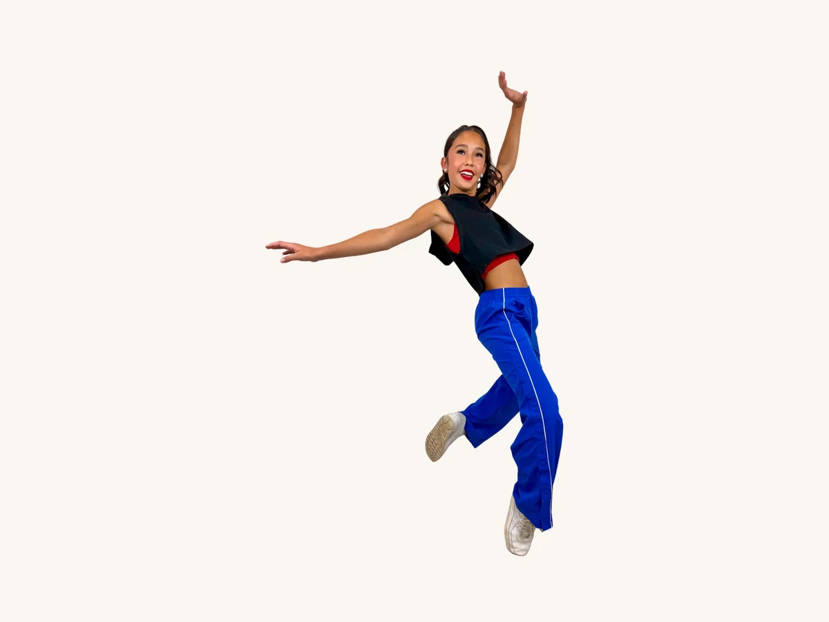 Adult dancer in a crop top and blue track pants mid-jump
