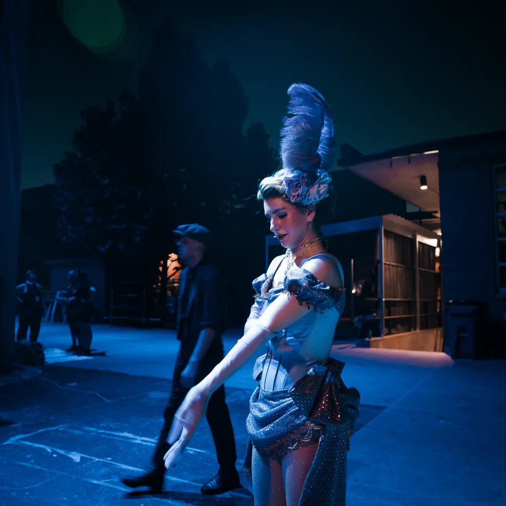 Becca Perron on a blue-lit stage in a feathered headpiece during Newsies