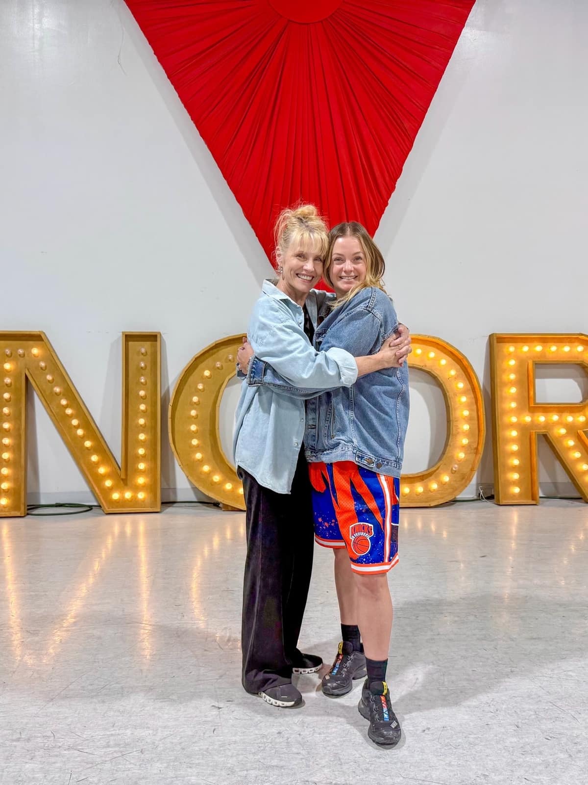 Two Encore instructors hugging in front of the studio marquee letters
