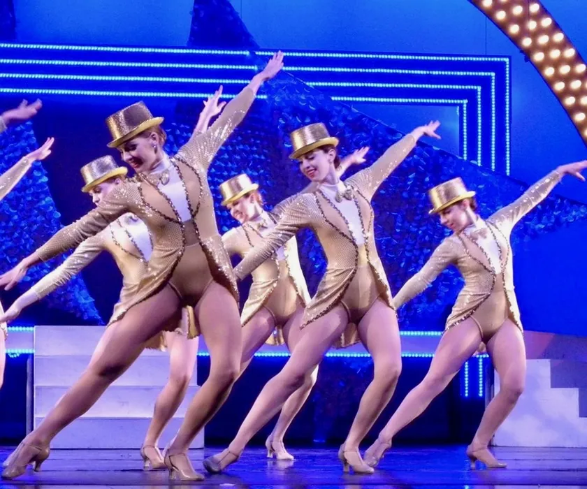 ETAP dancers in gold costumes and top hats in a kick line on stage