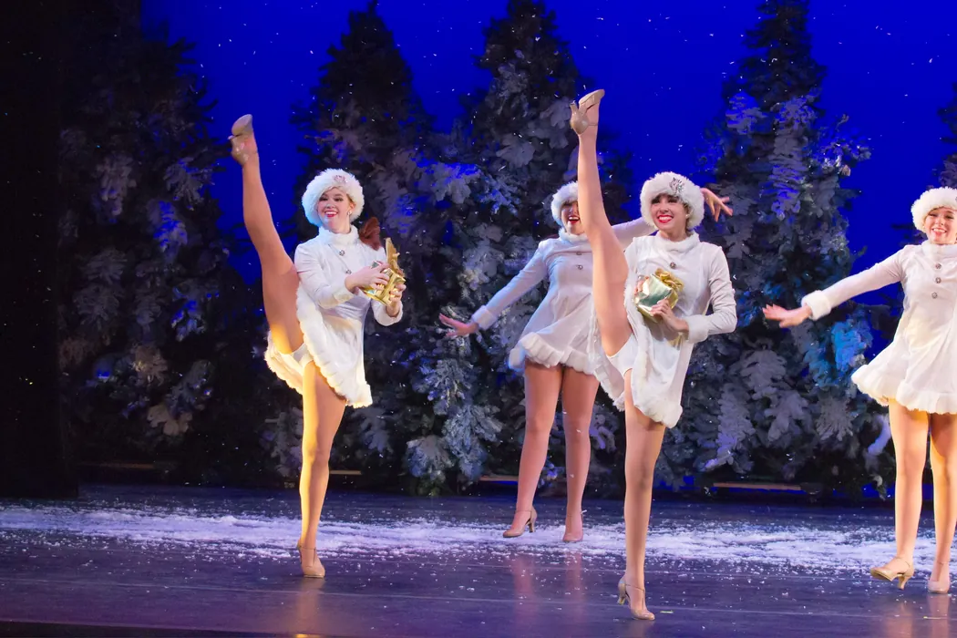 ETAP dancers in white costumes performing a winter number against a snow backdrop