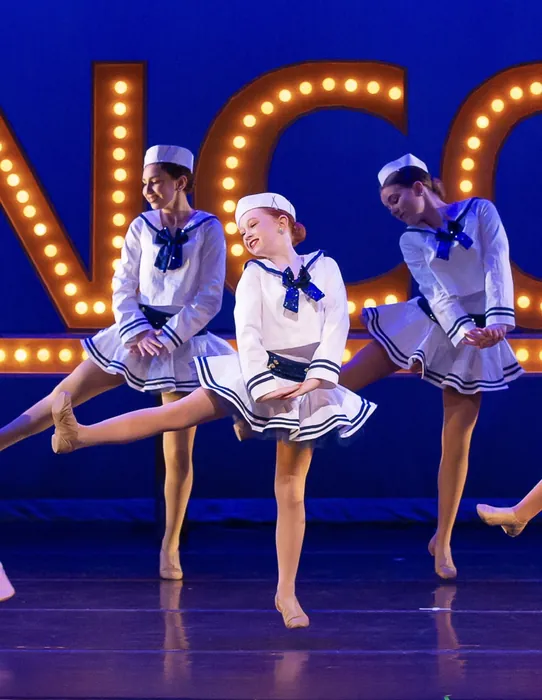 ITP dancers in blue and white costumes leaping in unison on stage