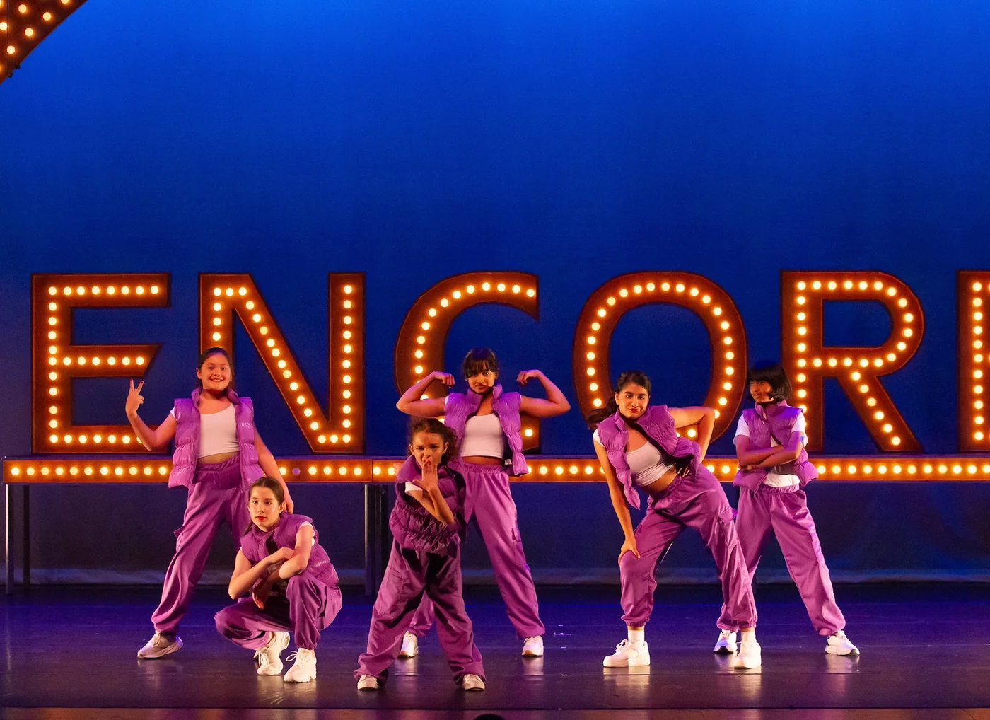 Junior dancers in tracksuits performing in front of the lit ENCORE letters