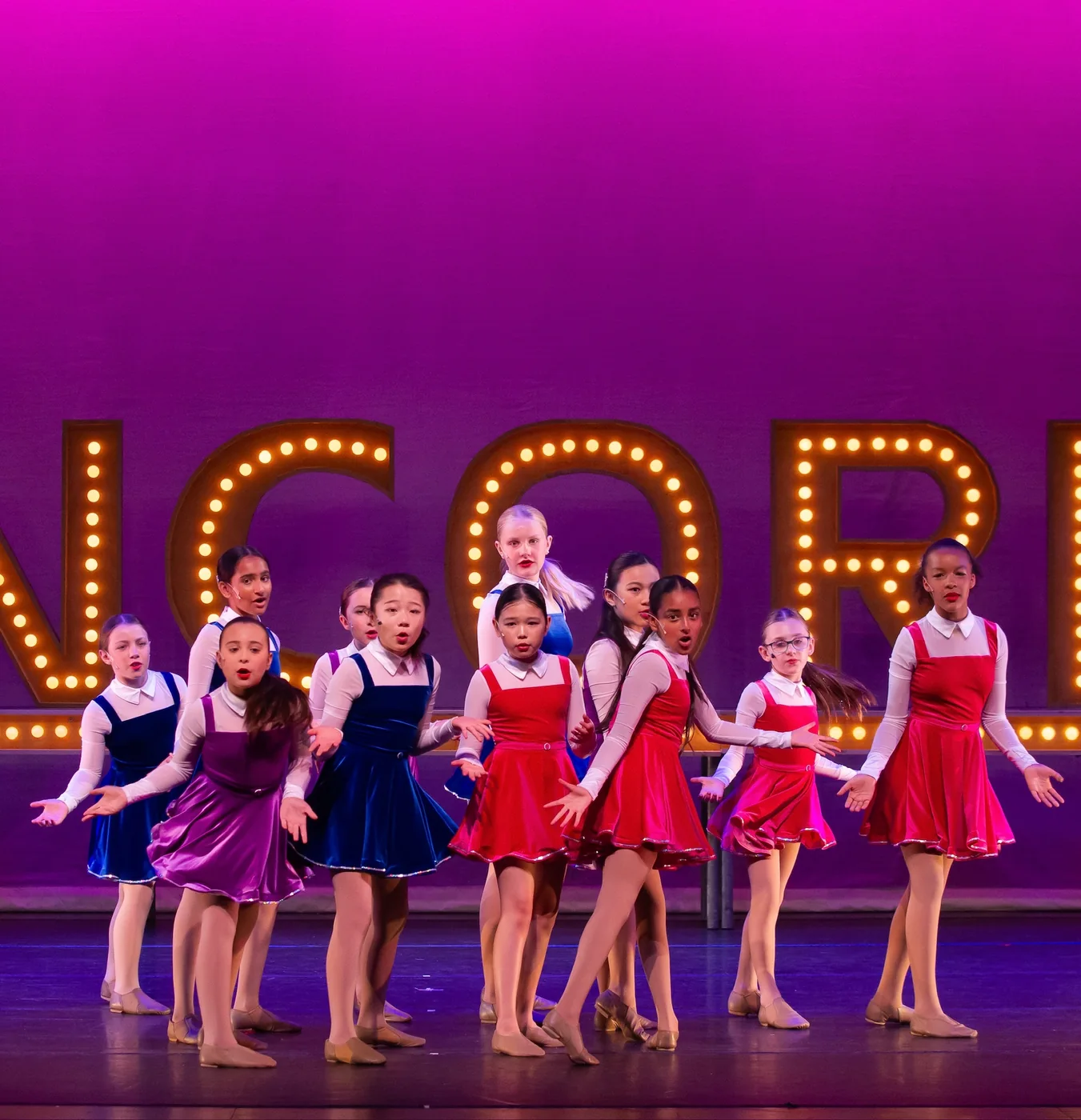 Junior dancers in navy and red costumes on stage before the ENCORE letters