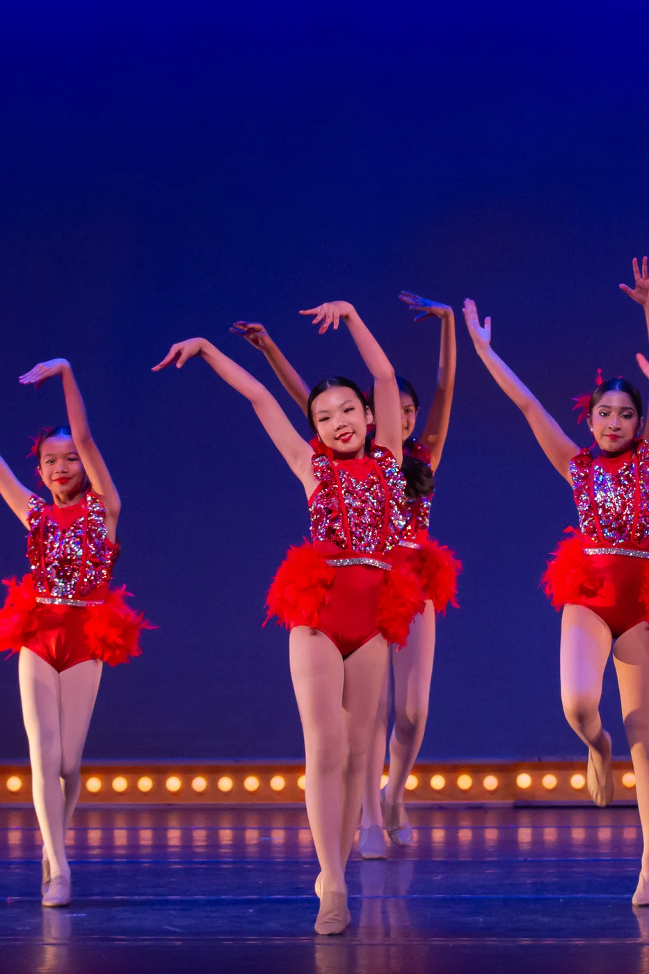 Junior dancers in red tutus finishing a number with their arms raised