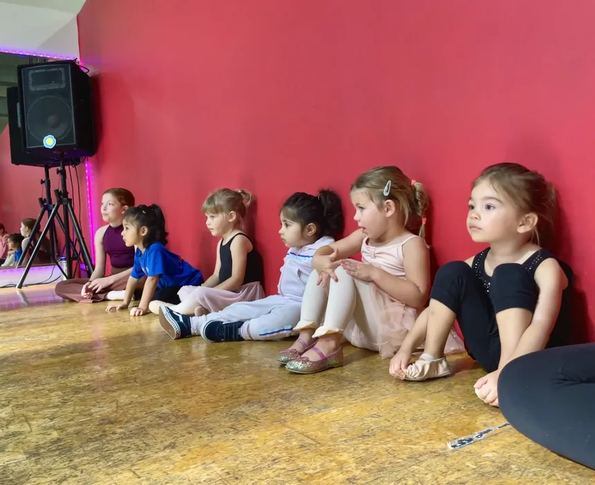 A row of Munchkin dancers sitting along the studio wall waiting for class to start