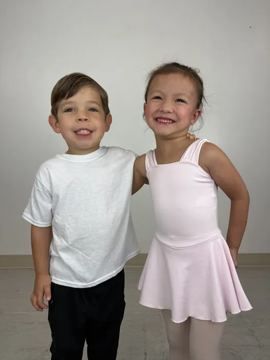 Two young Encore dancers in class attire standing arm in arm before their first class