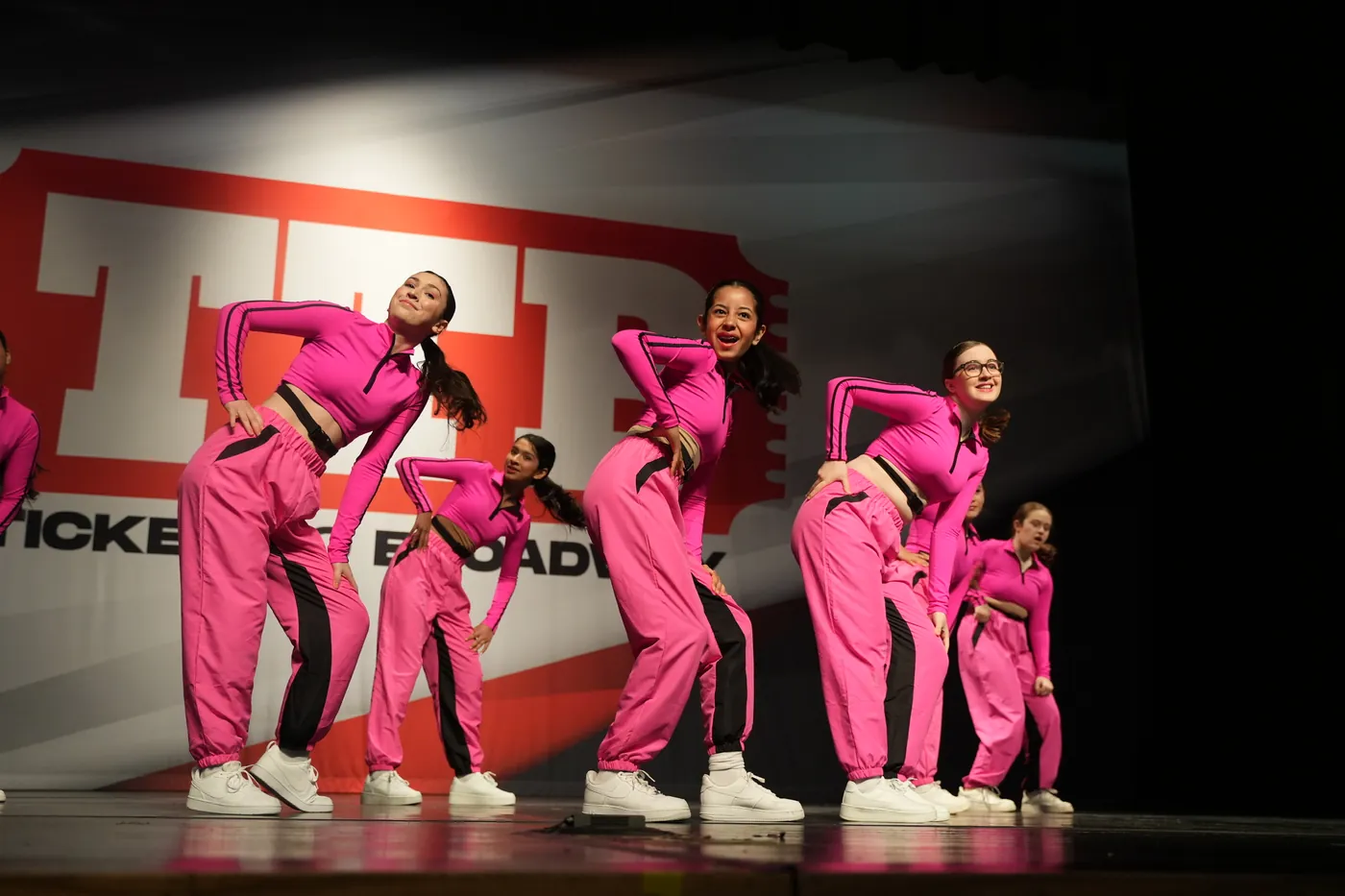 Encore Performance Team dancers in pink tracksuits posing in a line on stage