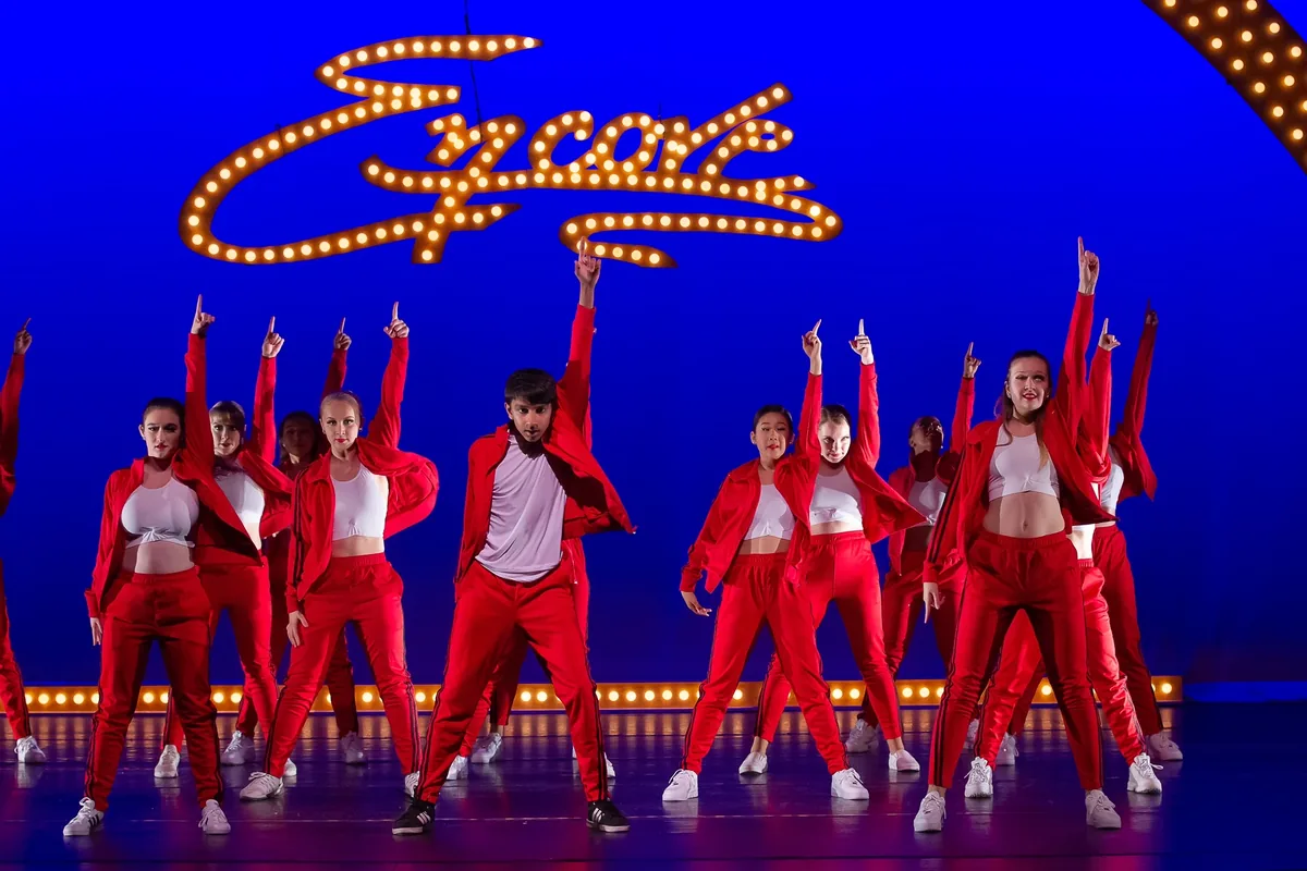 Dancers in red costumes performing beneath the lit Encore script sign