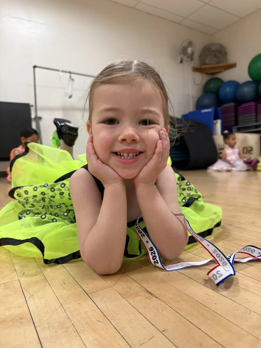 Young Encore dancer in a neon green costume resting on the studio floor before the show