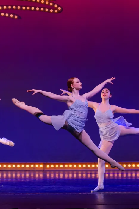 Teen dancer holding an arabesque on stage under the theatre marquee lights
